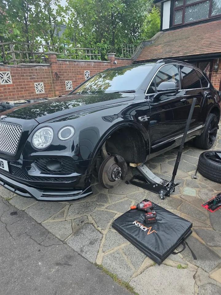 Black Bentley Bentayga on a trolley jack on a driveway, front wheel off and brake disc exposed